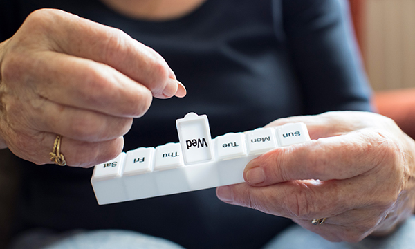 Picture shows older woman taking medication from a dosette box.