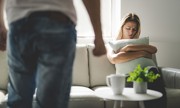 woman holds cushion defensively while man stands facing her