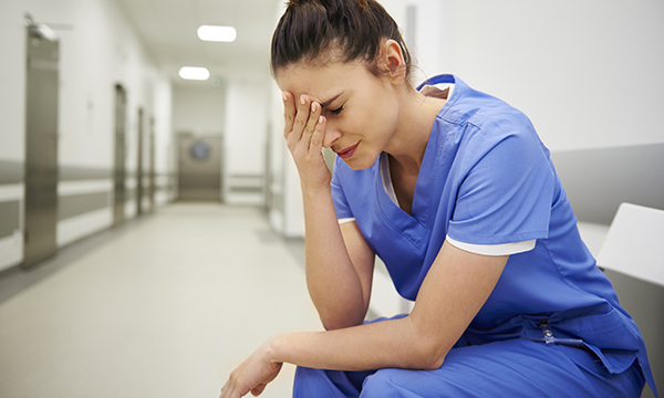 nurses sits in hospital corridor with her head in her hands as RCN calls for ministers to take responsibility for short staffing in the NHS