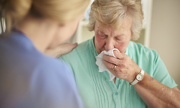 woman dabs her face with a tissue as nurse talks to her
