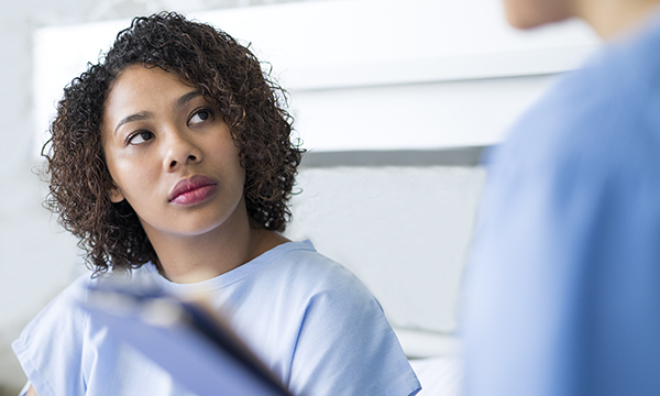 woman sitting in hospital gown looks up at healthcare professional
