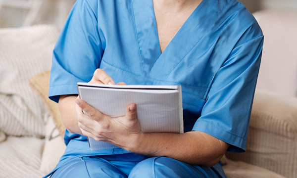 nurse dressed in scrubs writes in a note pad