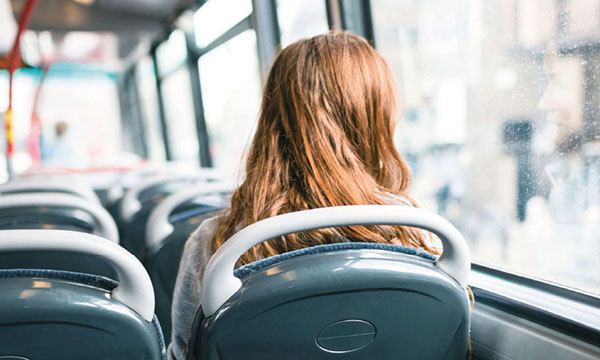 Image of a person sitting alone on a bus looking out the window, suggesting loneliness or sadness