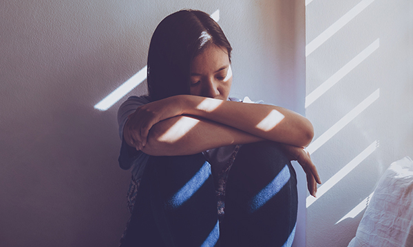 Picture shows a woman hunched over her knees, looking sad. A human group complains of missed NHS targets on moving patients with learning disabilities and autism to community-based settings.