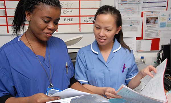 two nurses standing together, checking paper records