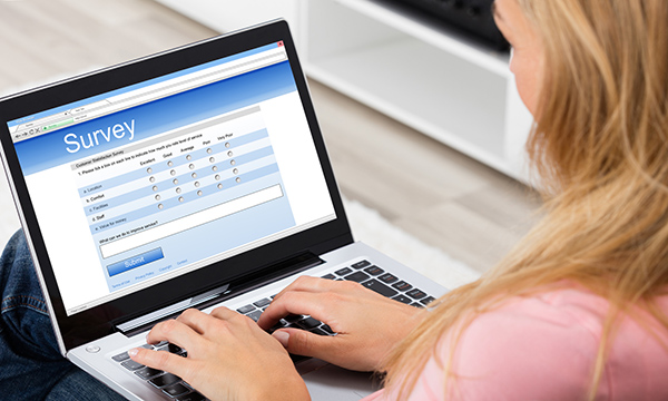 Picture shows a woman sitting at a laptop writing replies to a survey