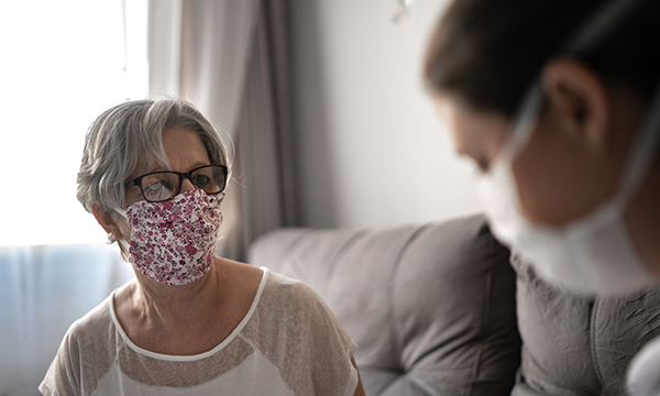 Picture shows a medic visiting a patient's home. Both are wearing masks.
