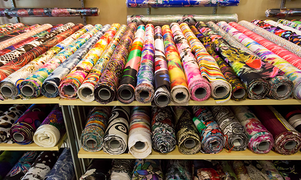 Picture shows a shelf with colourful bolts of fabric
