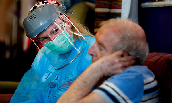 care home nurse wearing a face mask and visor talks to care home resident