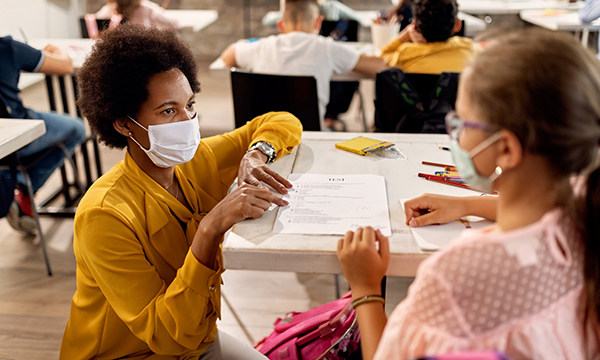 Picture shows a classroom with a female teacher talking to a schoolgirl