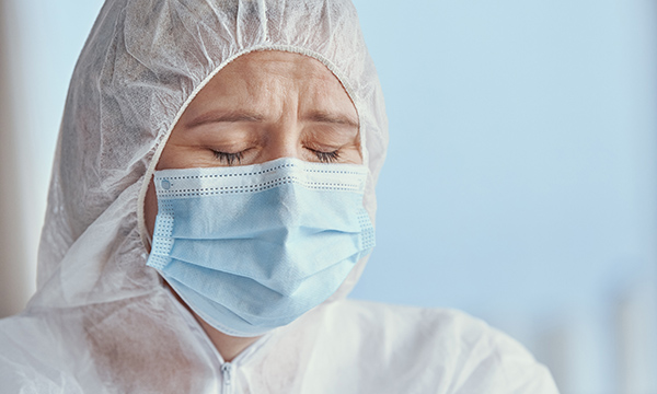 Picture shows a medic in personal protective equipment looking distressed
