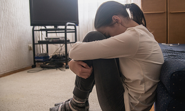 Picture shows a girl squatting on the flloor and hiding her face in apparent distressface