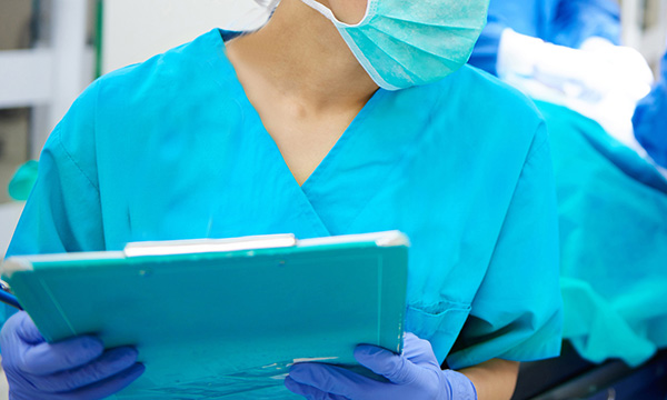Picture shows a medic wearing  face mask and filling in a form on a clipboardv