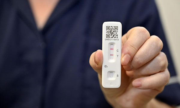Picture of a medic holding a lateral flow test cartridge showing a positive result 