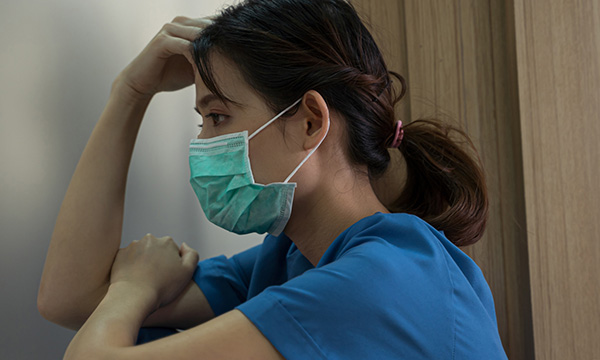 Picture shows a young female Asian nurse staring at a wall and looking sad