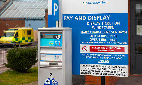 A hospital car park pay meter with a sign detailing parking charges