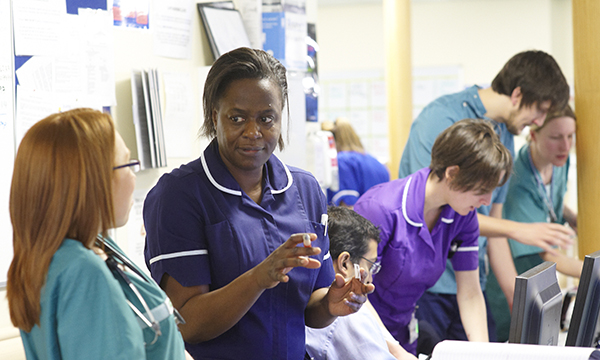 Nurses in crowded ward setting, some talking, others checking notes
