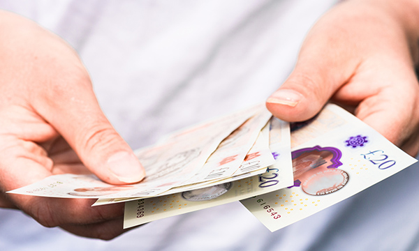 Photo of someone counting £10 and £20 notes in their wallet: the NMC has frozen its registration fee to £120 for another year