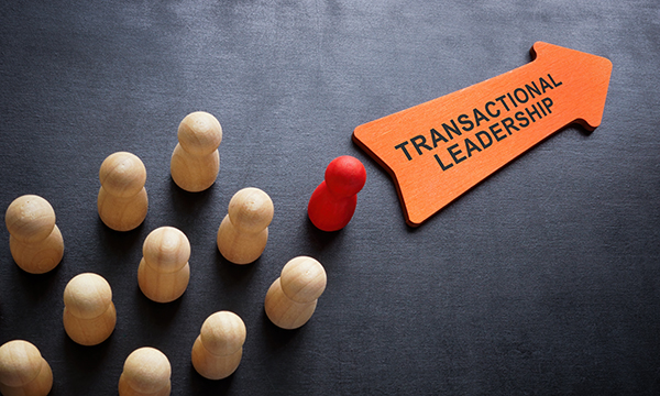 ‘Transactional leadership’ written on an arrow, with ranks of wooden figures in its wake, the foremost one painted red: Transactional leadership can help achieve short-term goals and provide clear direction and structure
