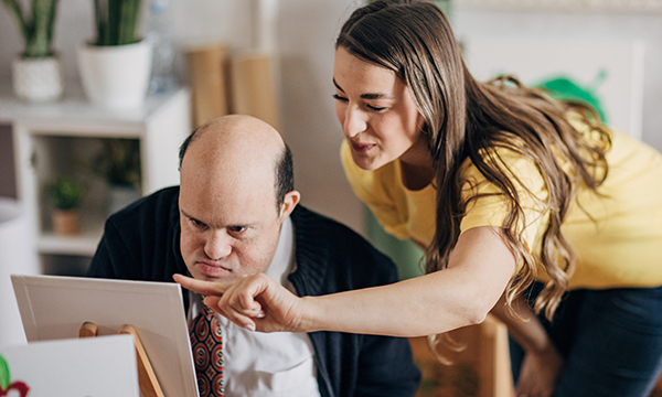 A man who has a learning disability is given some guidance on painting on canvas by a tutor during an art healthcare workshop