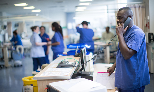 Photo of nurse answering phone on a busy ward. A new report calls for more managers to free up nurses' time to care for patients