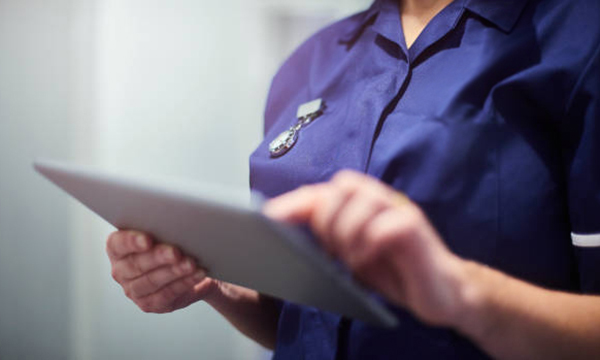 A nurse, face unseen, checks information on a tablet computer