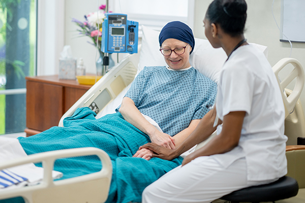 Nurse sits at bedside with a patient and holds her hand