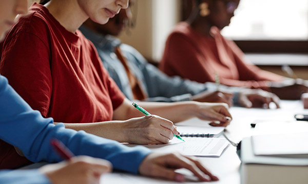 Students sitting in a row writing notes at a large desk, illustrating financial support announced for nursing students in Wales