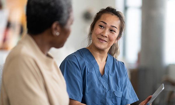 A nurse smiles at a patient as she shows her some information on a tablet