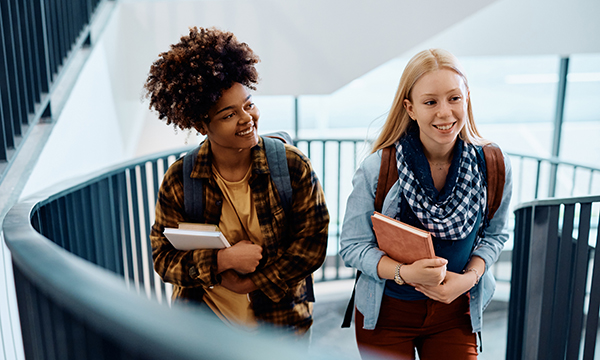 Two young women, with books in their arms, walk up a staircase – as nurse academics call for politiicans to prioritise nursing student recruitment