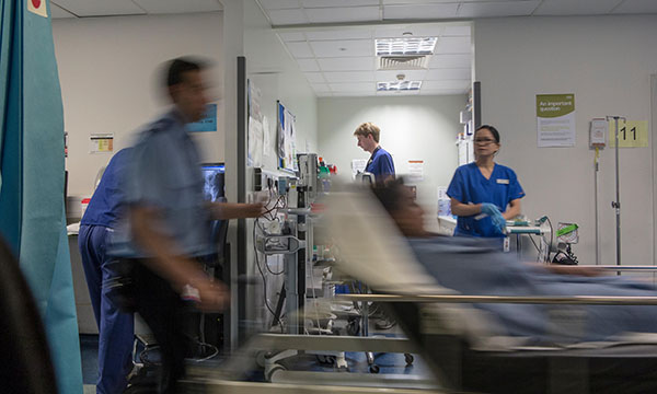 Scene at a busy hospital with medics engaged in various tasks as a trolley with a patient on it is pushed past
