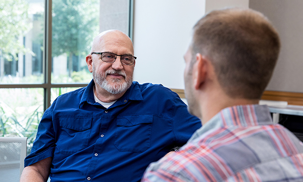 A man smiling contentedly as he sits and has a conversation with another man