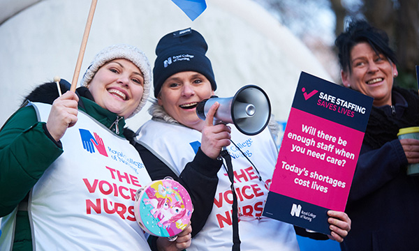 Striking nurses look happy standing outside the Northern General Hospital in Sheffield. One holds a 'sage staffing' placard and speaks into a loud hailer