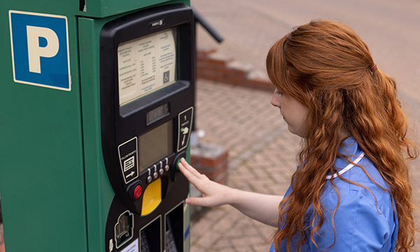 A nurse in uniform using a car park ticket machine