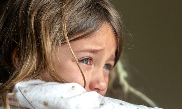 A young child looks into the distance with tears rolling down their cheek