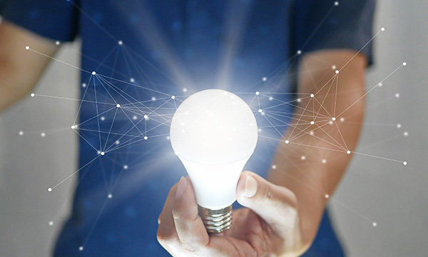 Nurse, face unseen, holds an illuminated lightbulb, with systematically connected dots appearing to radiate from, illustrating the capacity of nurses to be innovative