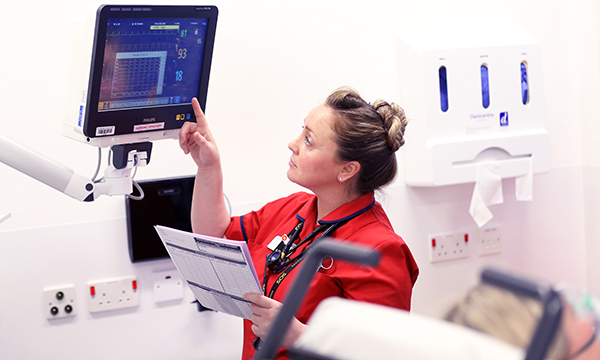 Nurse reads a vital signs monitor at patient’s bedside. This is key information when assessing level of risk for a person with sepsis