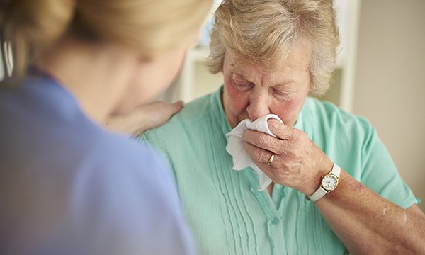 A tearful older woman is consoled by a nurse