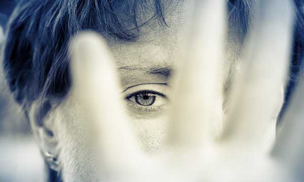 Close-up of the face of a woman who is holding up her hand with fingers spread in a protective gesture