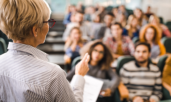 A female lecturer stands at the front of a lecture theatre teaching nursing students