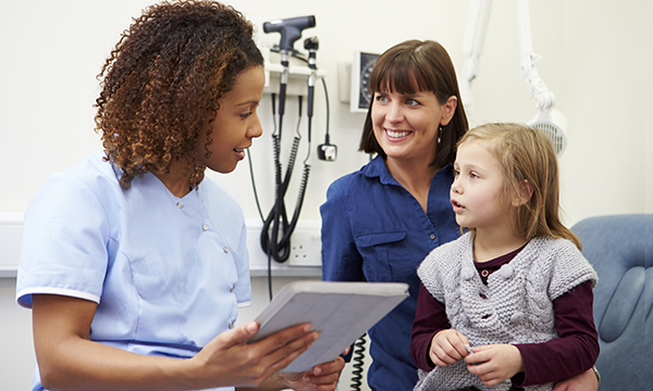 A general practice nurse holding her notes talks to a woman and child