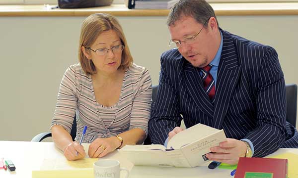 Two officials sit together conferring over paperwork to show the FtP process that is currently subject to planned changes that could reduce need to go to formal hearings