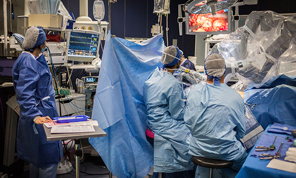 Image shows two surgeons watching a screen as they perform robotic prostate surgery on a patient in an operating theatre, with nursing staff in attendance