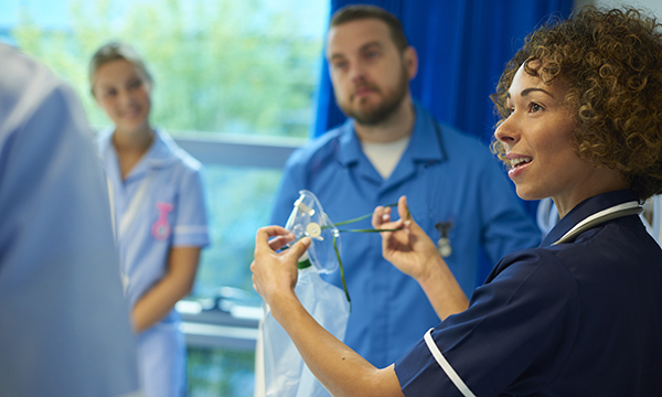 A senior nurse gives a demonstration using an oxygen mask to other nurses