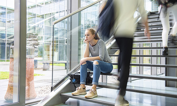 A depressed and fed up looking nursing student site on the stairs of college