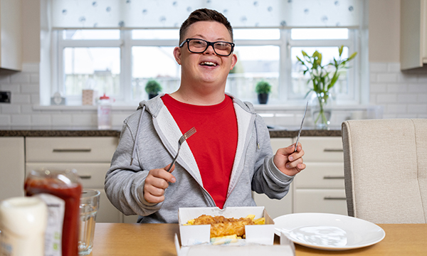 A young man smiling as he gets ready to eat a meal of fish and chips