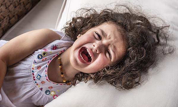 A distressed young girl lying on a bed and howling in pain