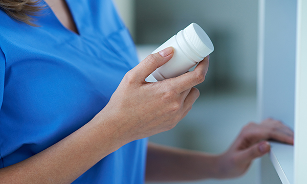 Image shows a member of healthcare staff facing an open cupboard and holding a plastic bottle of medication