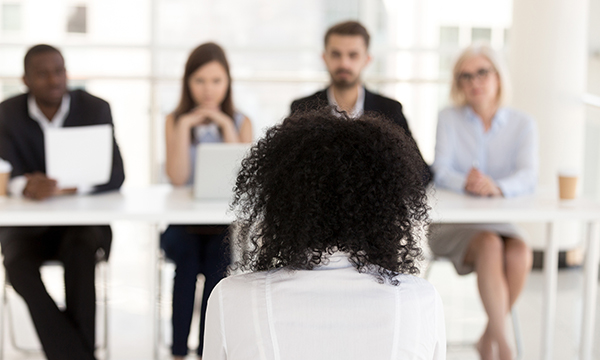 A woman, viewed from behind, facing professional panel of four, to illustrate NMC FtP panel process