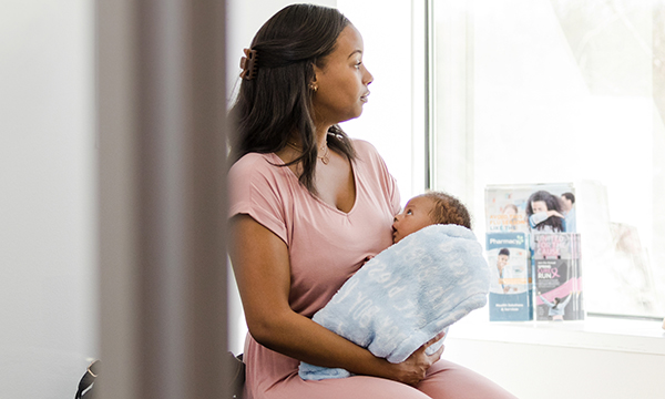 Postpartum psychosis: a young woman holding a baby in her arms sits next to a window looking outside
